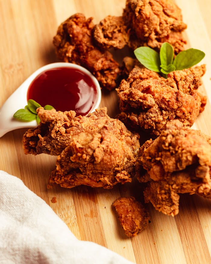 fried-chicken-with-sauce-and-a-spoon-on-a-cutting-board-17282046 Delicious crispy fried chicken served with a tangy dipping sauce on a wooden board.