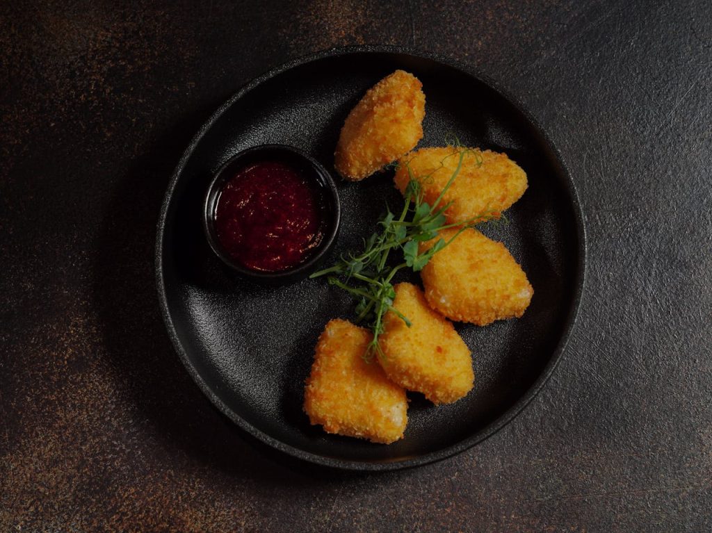 fried-meat-with-a-bowl-of-dipping-sauce-20535805 Golden fried nuggets served with a tangy dipping sauce on a black plate, garnished with fresh herbs.